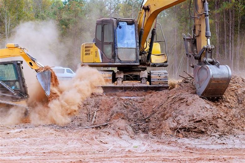 Two yellow excavators digging in dirt, raising dust in a construction site.