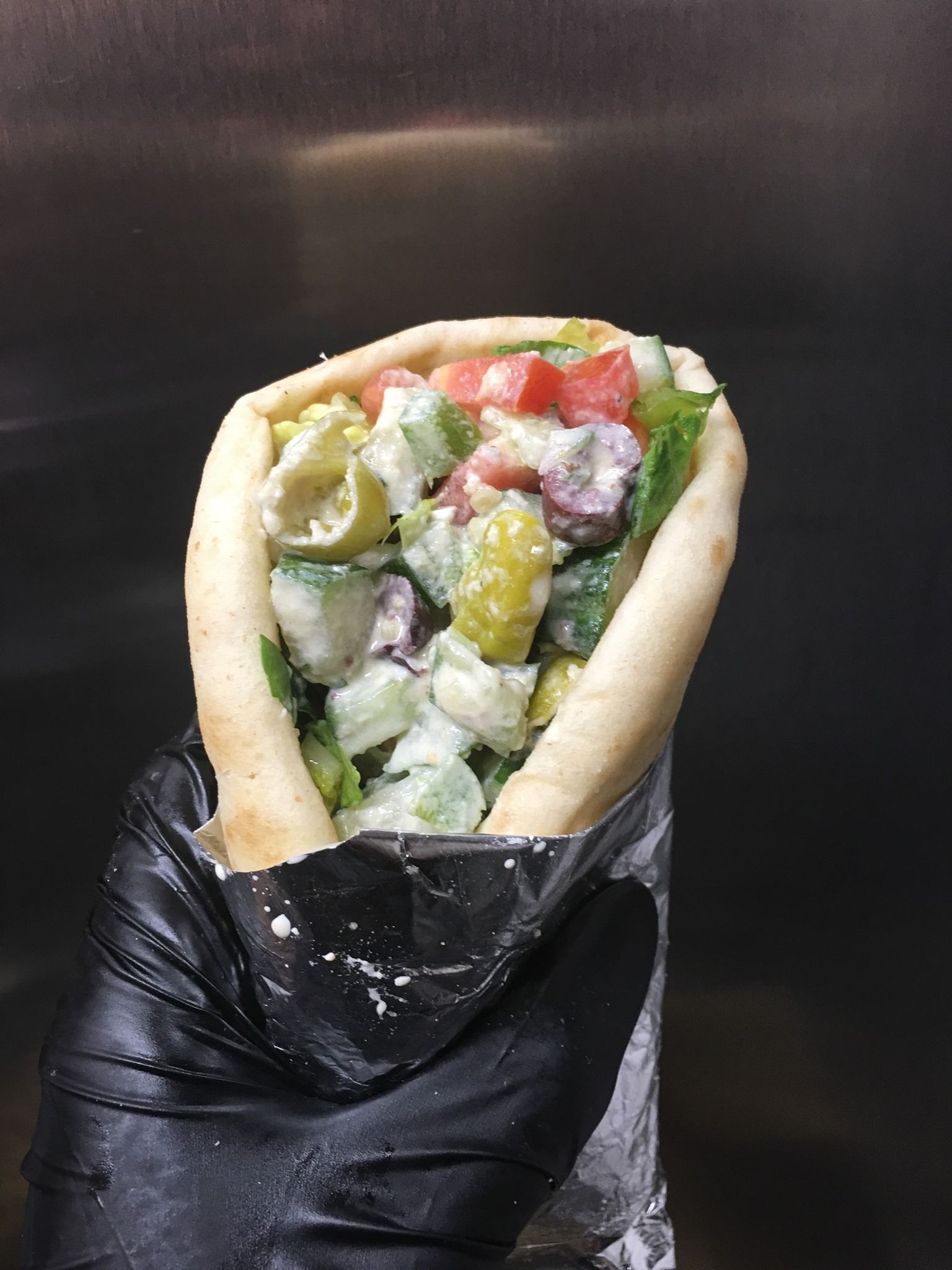 A person is holding a pita sandwich wrapped in plastic wrap.
