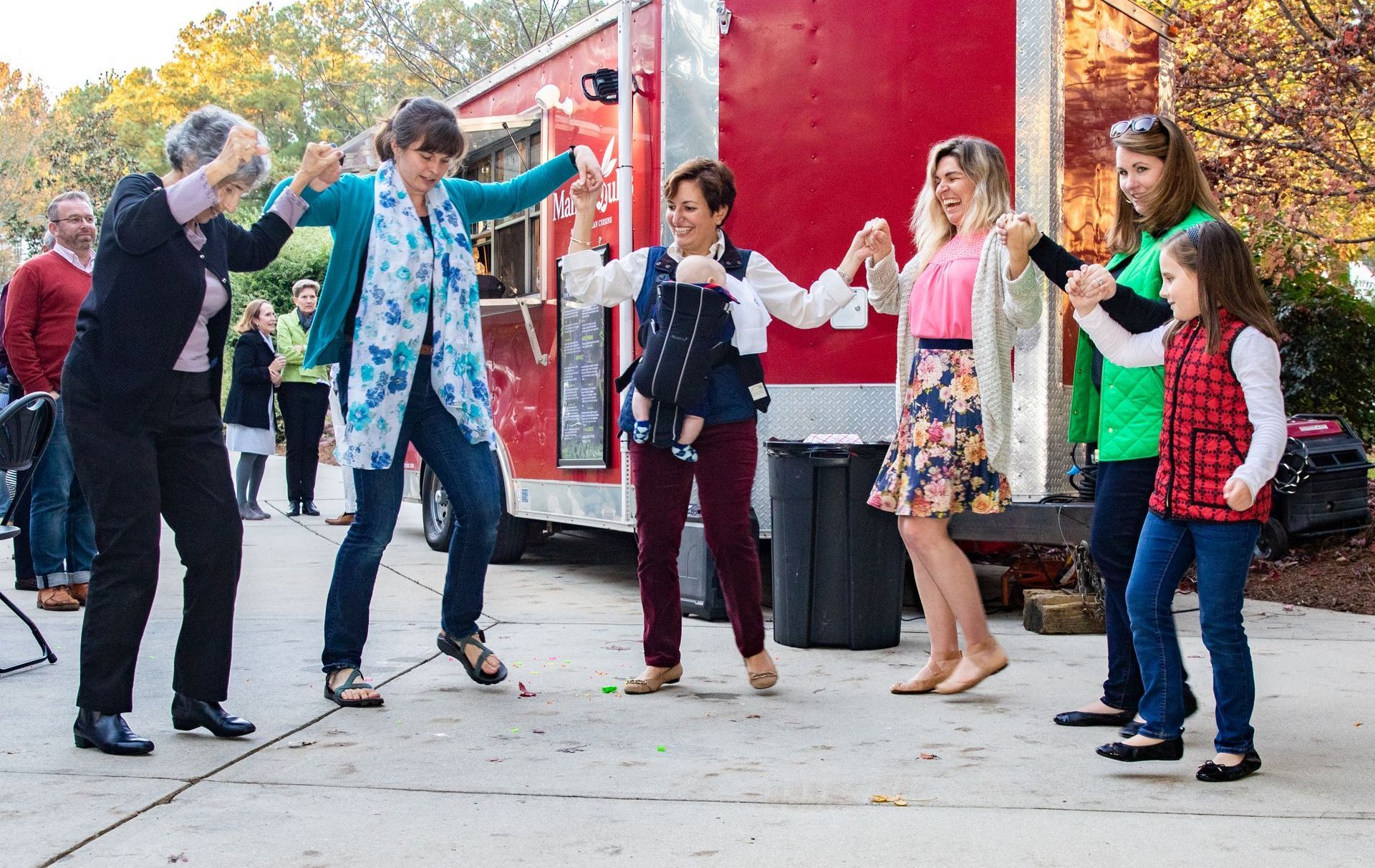 A group of people are dancing in front of a food truck.