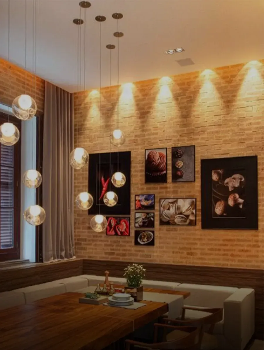 Sala de jantar com parede de tijolo inglês, obras de arte, luminárias pendentes, mesa de madeira e assentos embutidos.