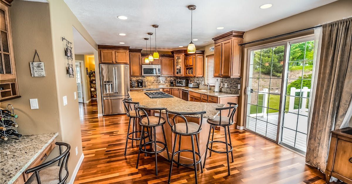 A kitchen with hardwood floors , stainless steel appliances , a large island and stools.