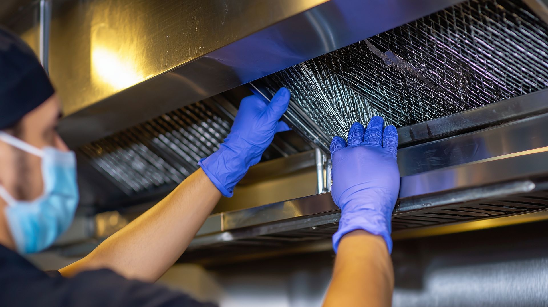 Worker in blue gloves cleaning a kitchen range hood filter with a brush