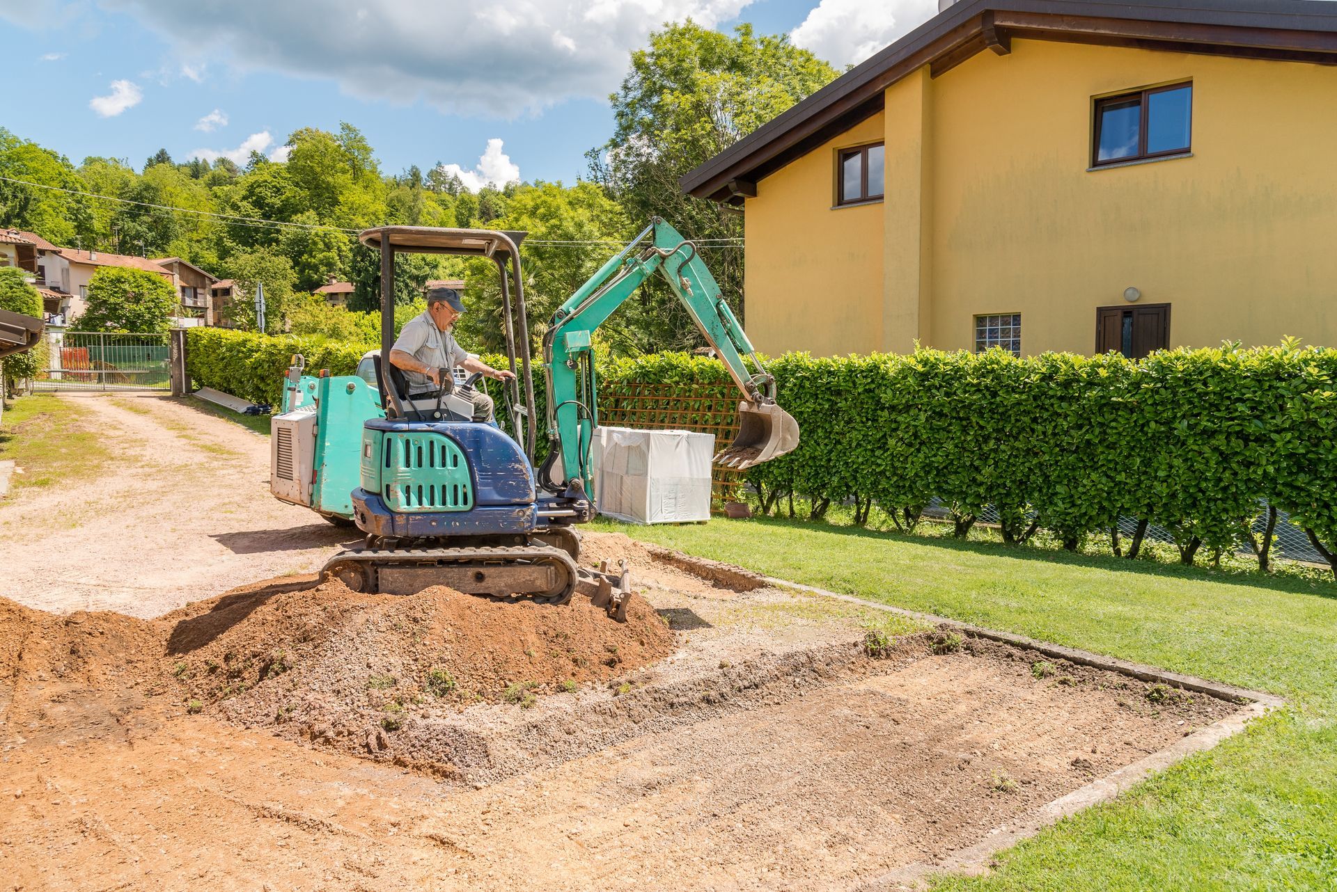 A worker on a mini excavator is digging the ground ahead of the house. Groundwork and exterior paving.