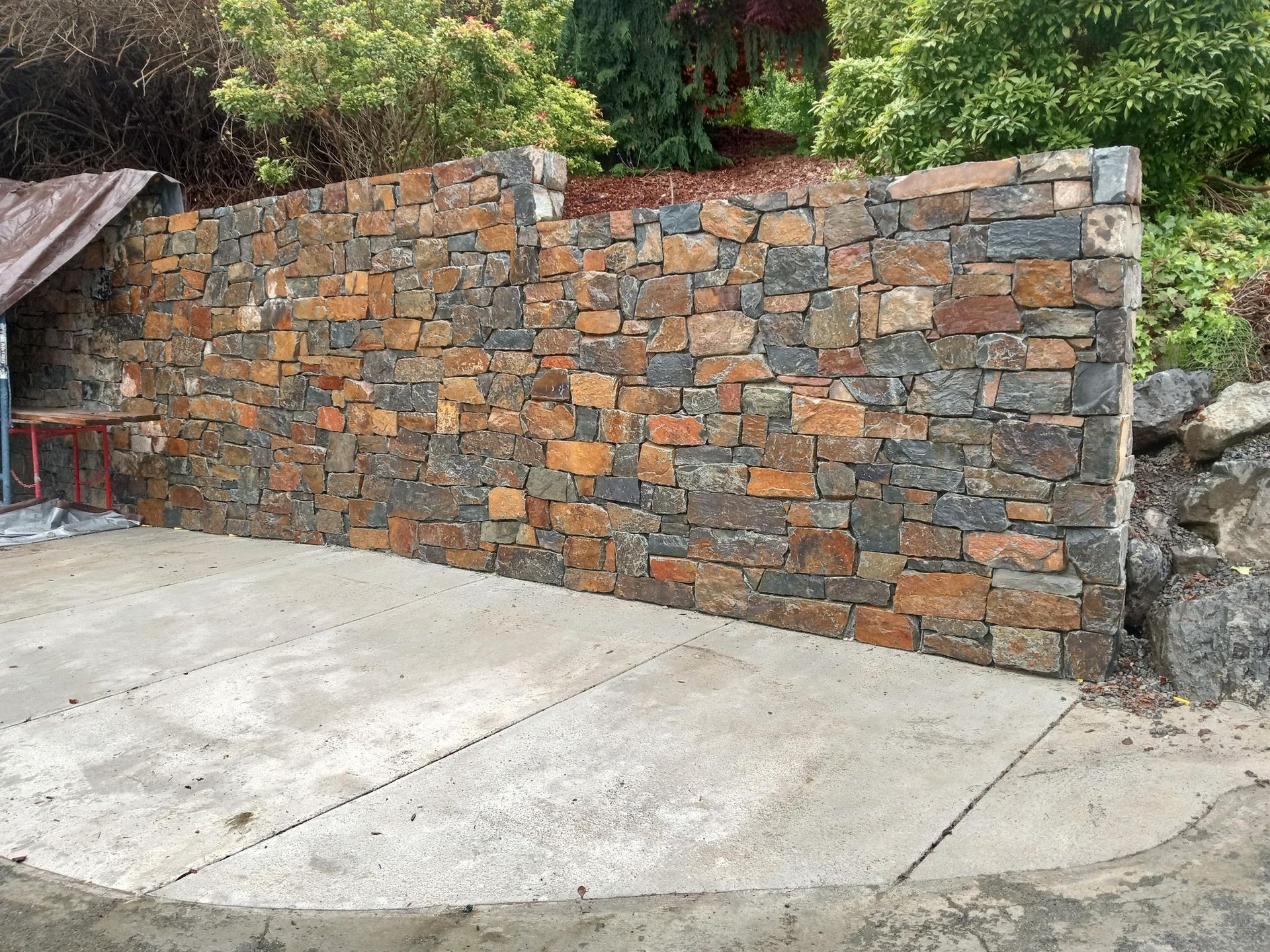 A large stone wall is surrounding a concrete driveway.