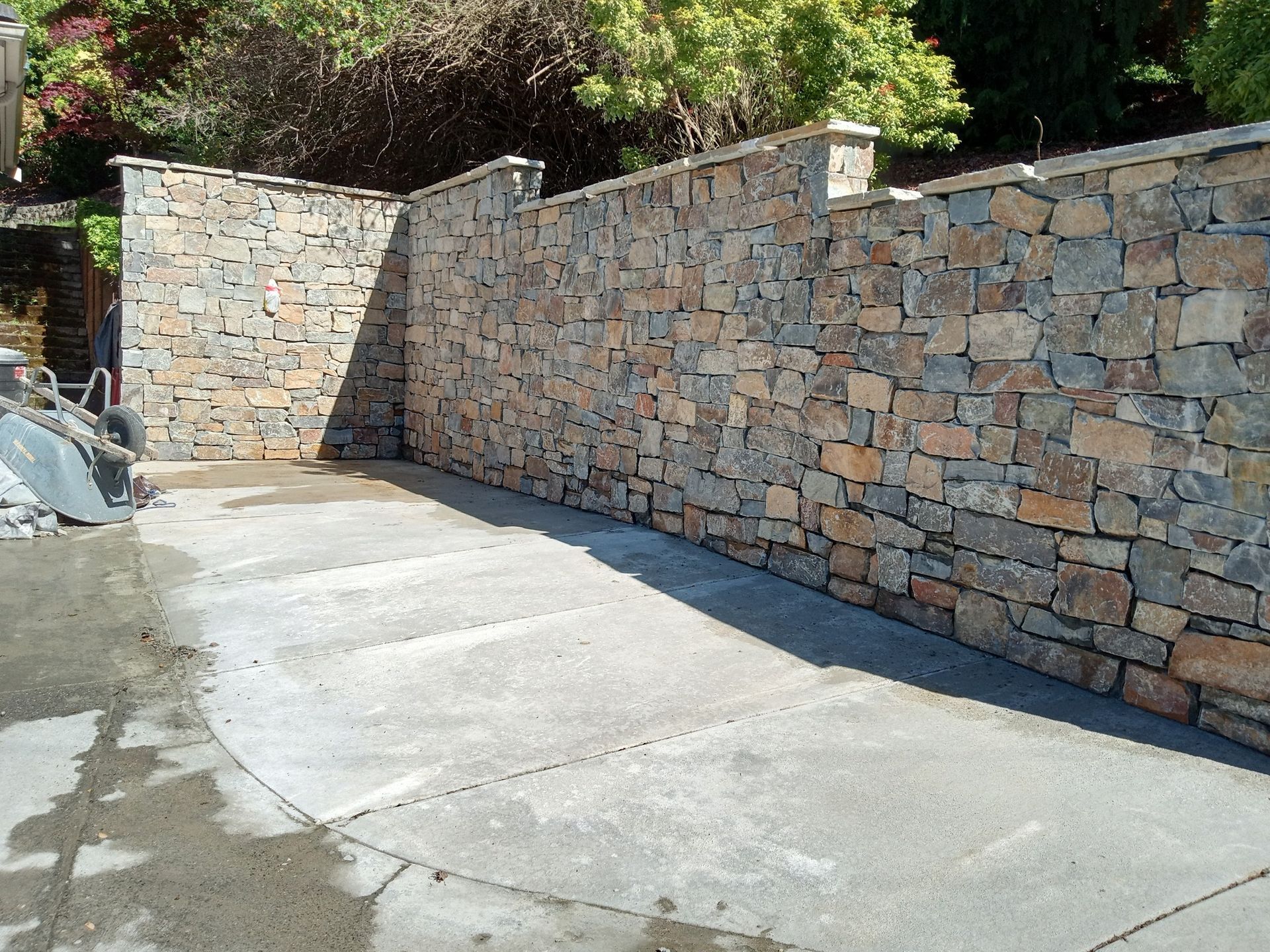 A large stone wall is surrounding a concrete driveway