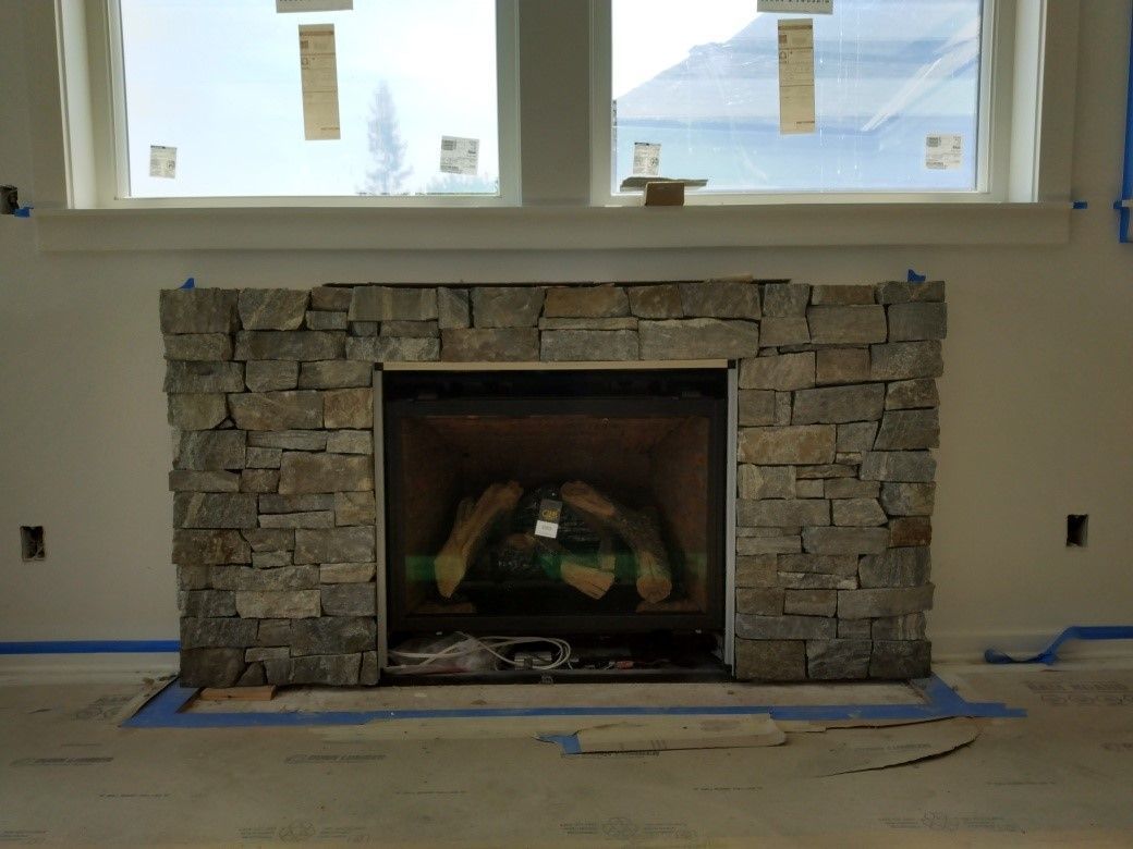 A stone fireplace is sitting in a living room next to a window.