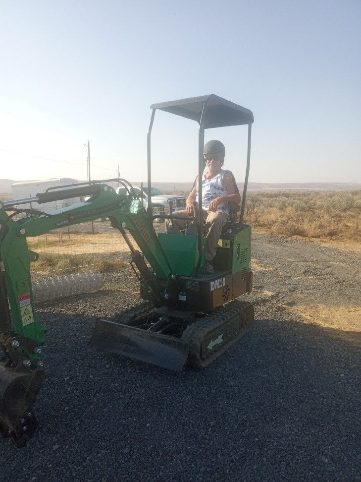 A man is sitting in a small green excavator on a gravel road.