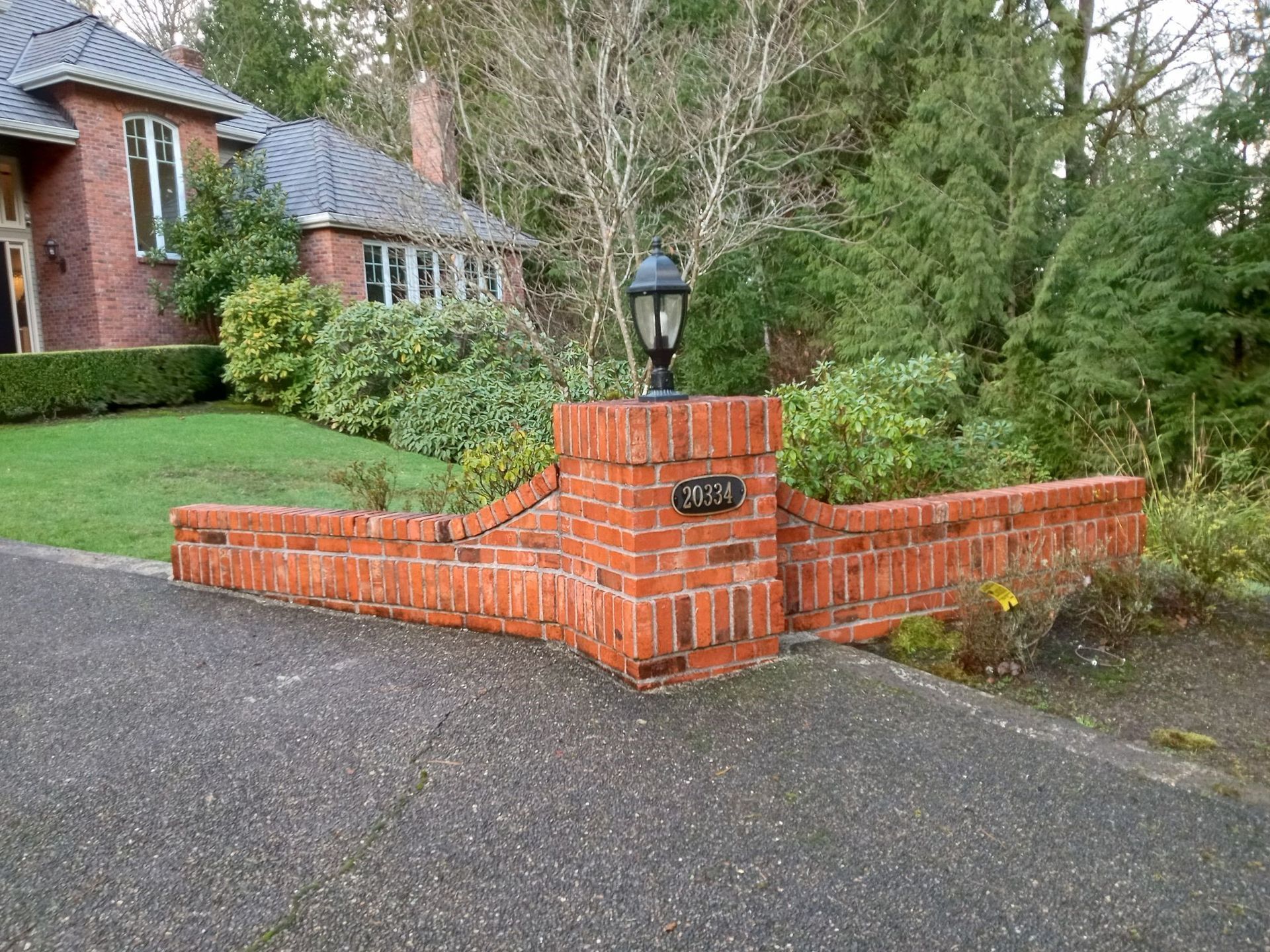 A brick wall with a lamp and a house in the background