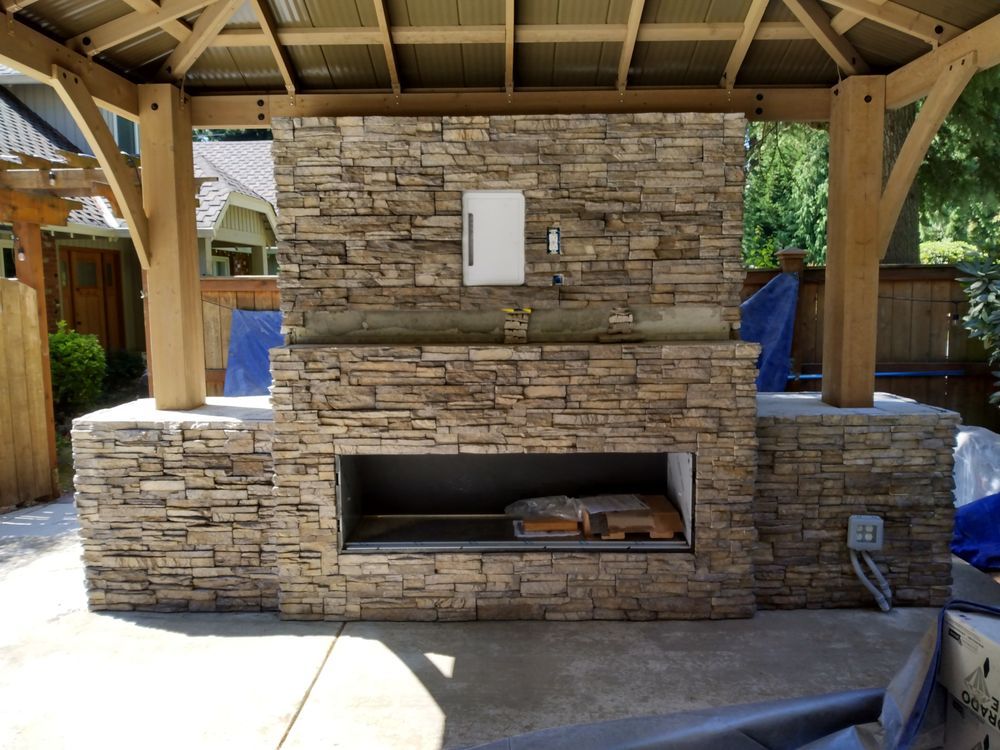 A large stone fireplace under a wooden gazebo
