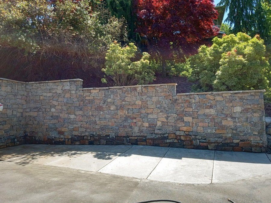 A stone wall surrounds a driveway with trees in the backgrounde I