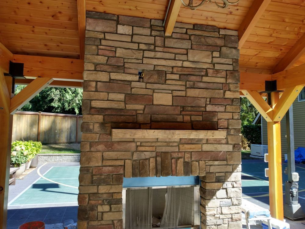 A large stone fireplace under a wooden roof with a basketball court in the background.