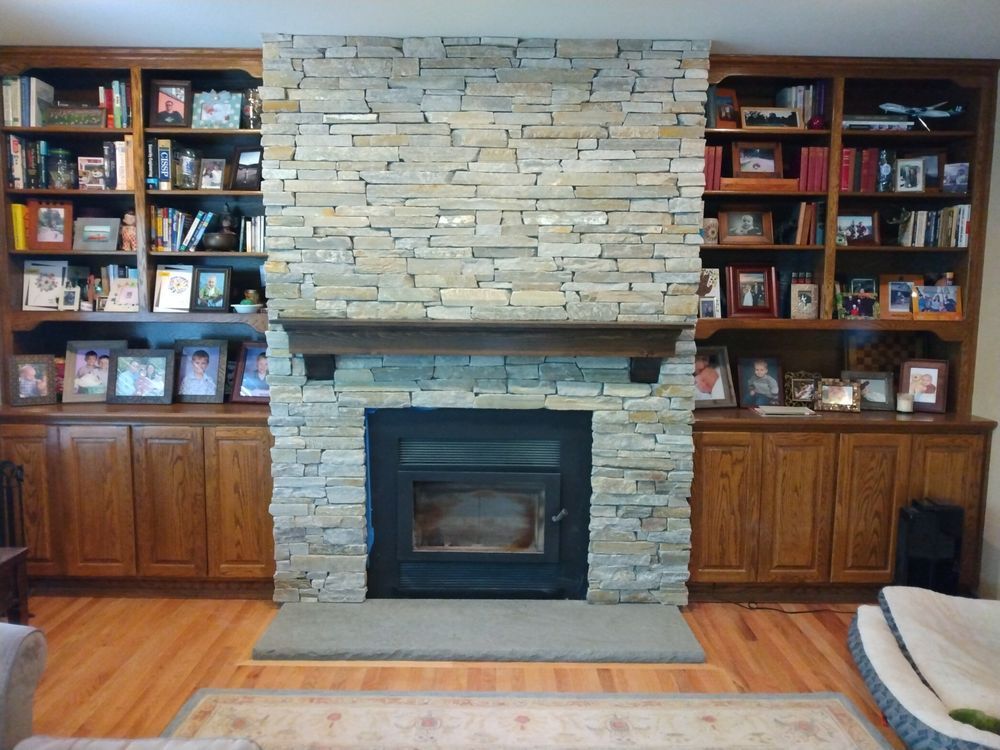 A living room with a stone fireplace surrounded by bookshelves and pictures