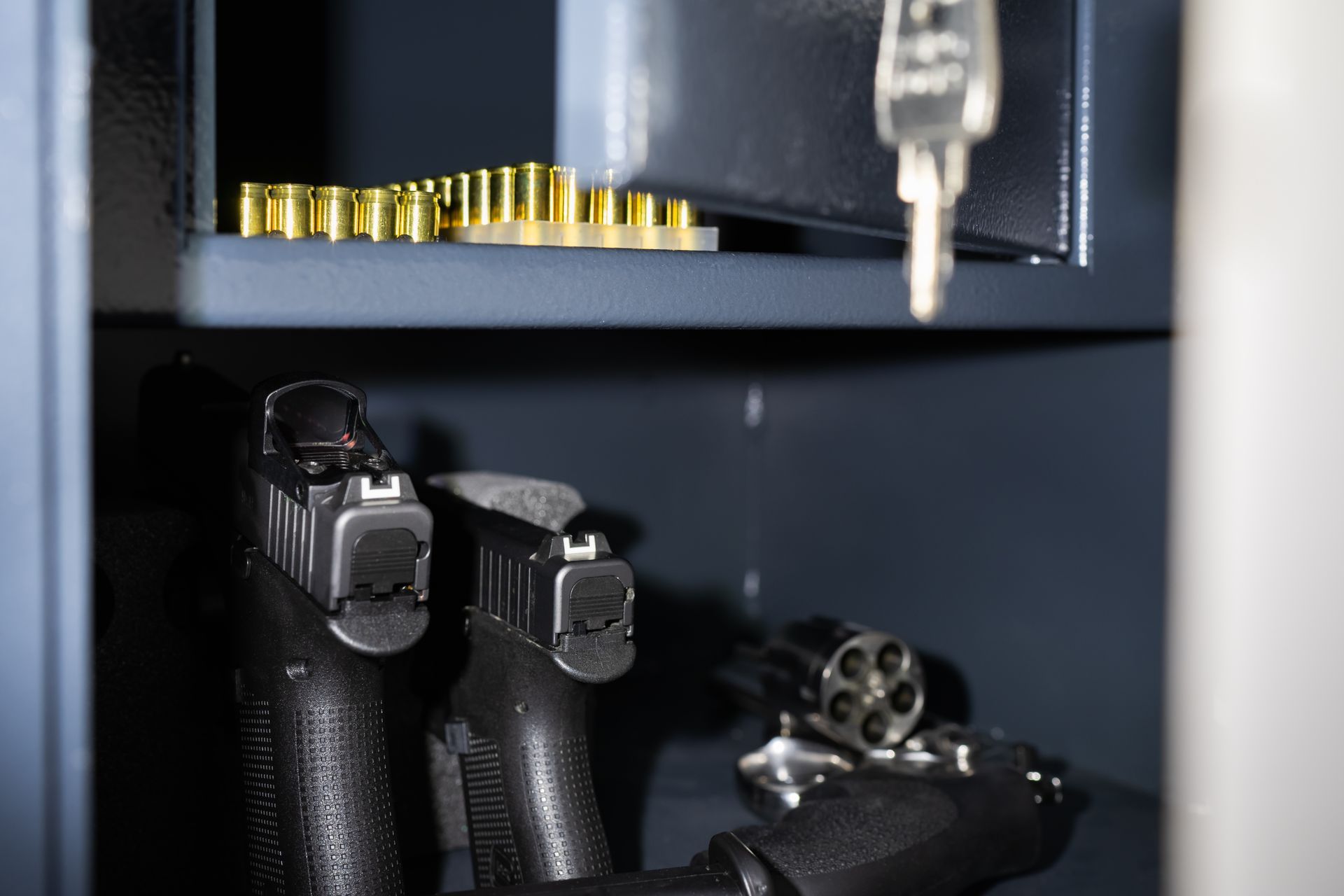 Guns inside a safe. Two black pistols and a revolver are visible, along with shell casings and a key.