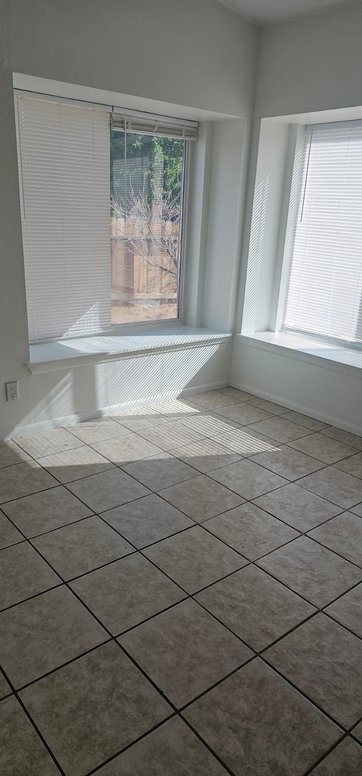 An empty room with tile floors and a window with blinds.