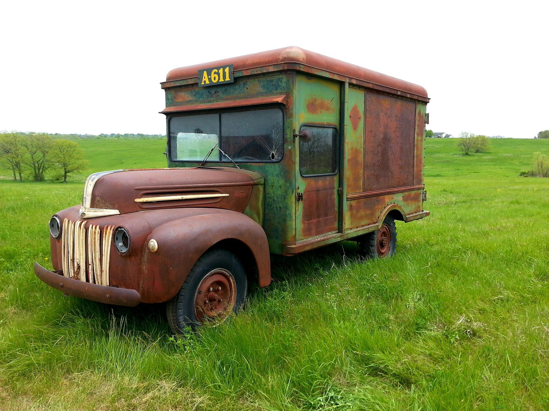 Rusty vintage green and brown truck in a grassy field.