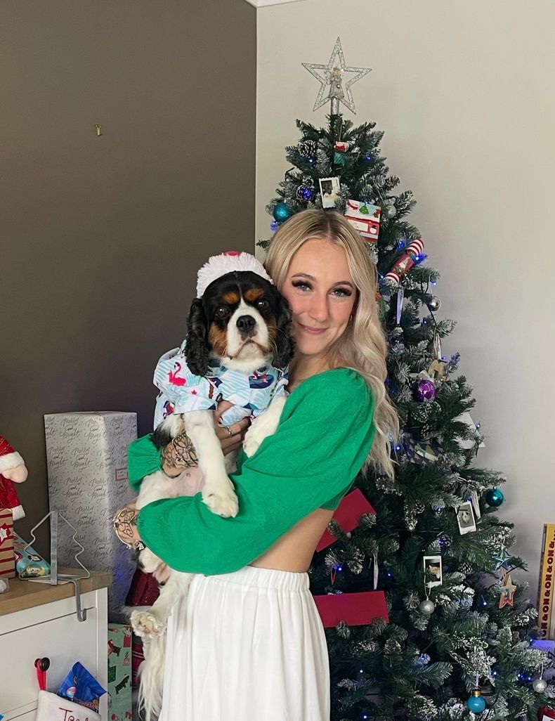 A woman is holding a dog in front of a christmas tree.