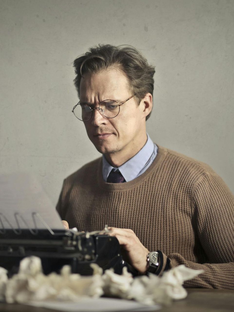 A man wearing glasses is typing on an old typewriter.