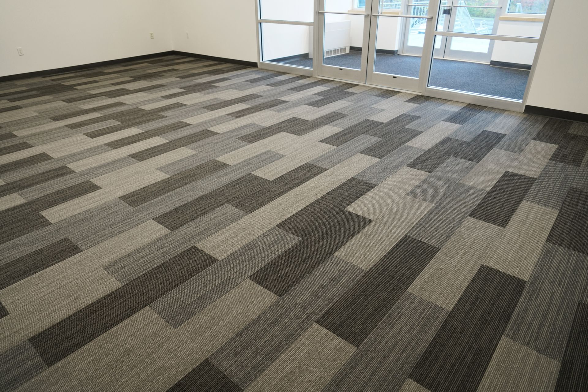 Gray and dark gray patterned carpet flooring in a room with glass doors.