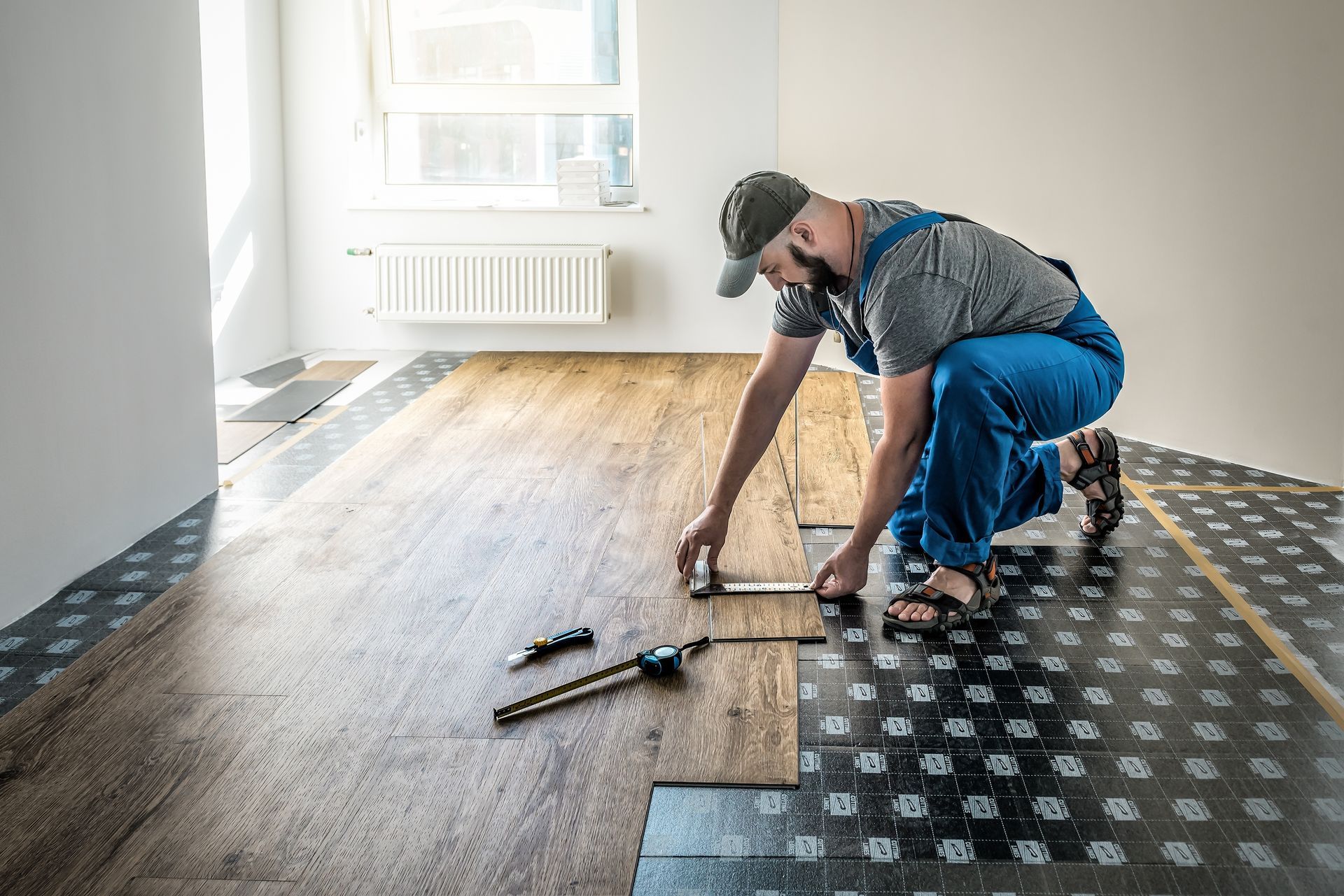 A worker installing wood flooring in a room. He is kneeling with tools nearby.
