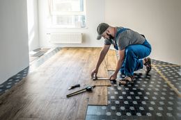 Man installing wood flooring in a room, measuring a plank.