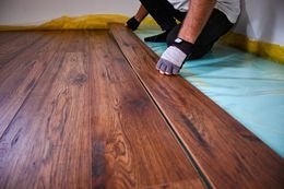 Person installing dark wood laminate flooring.