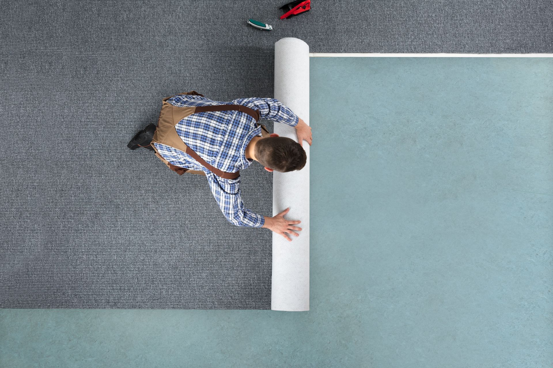 Overhead view of a person rolling out gray carpet onto a light blue floor.