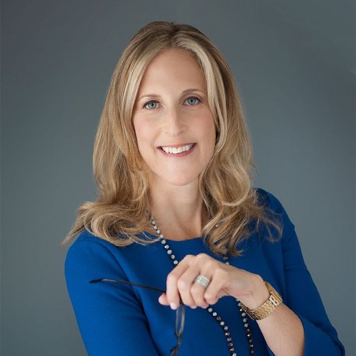 A woman with blonde hair and blue eyes is smiling for the camera