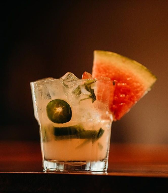 A close up of a cocktail with watermelon and jalapenos on a table.