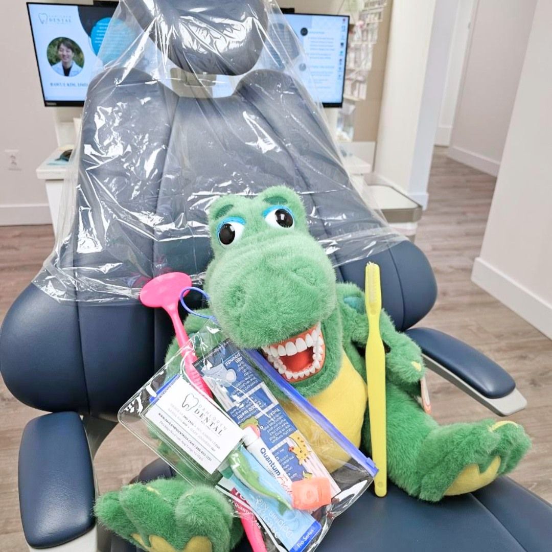 A stuffed dinosaur is sitting in a dental chair holding a toothbrush and toothpaste.