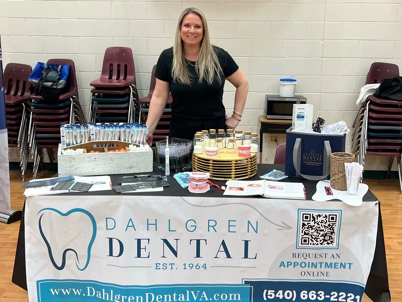 A woman stands behind a table with a banner that says dahlgren dental