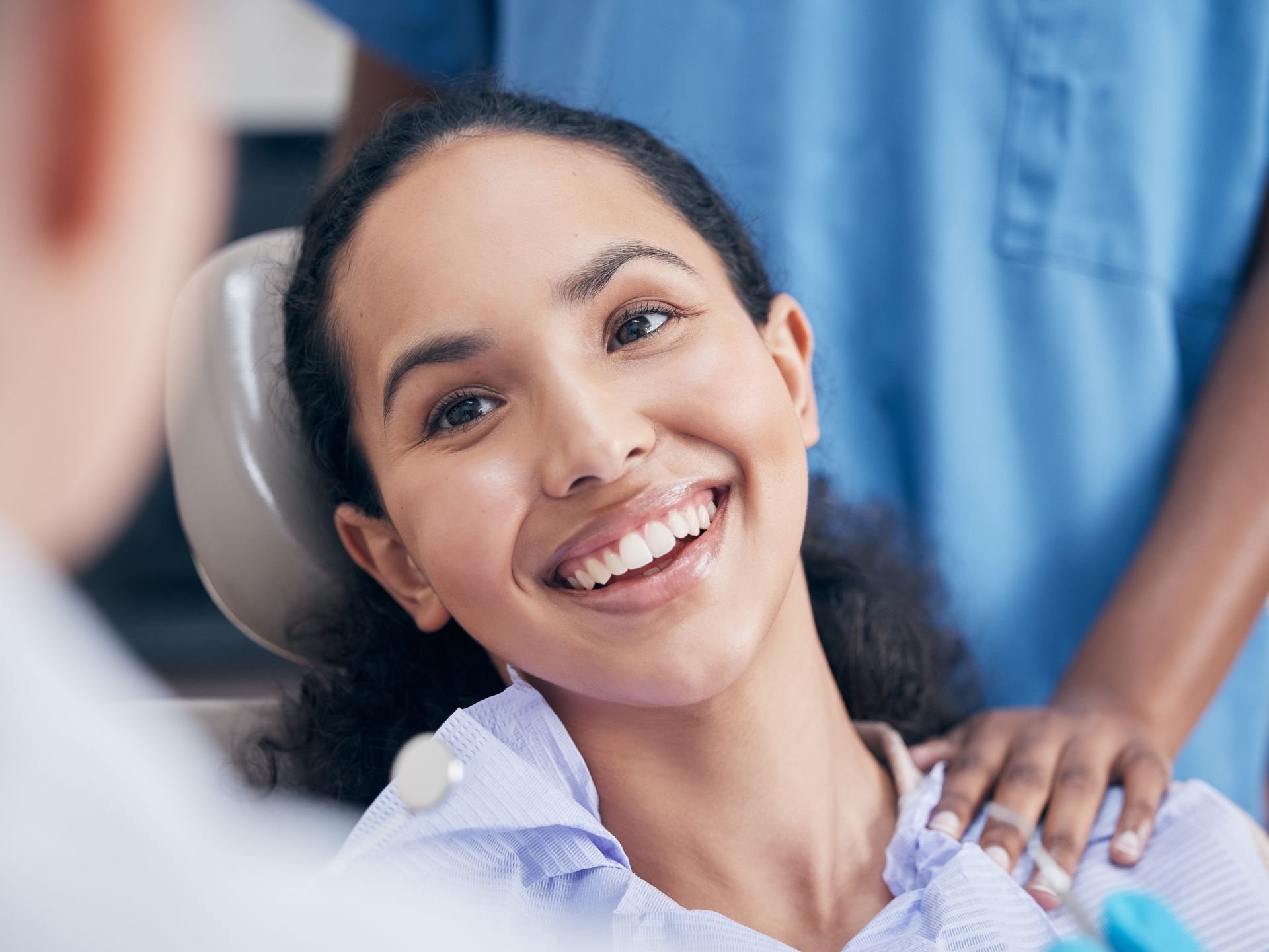 A woman is smiling while sitting in a dental chair.