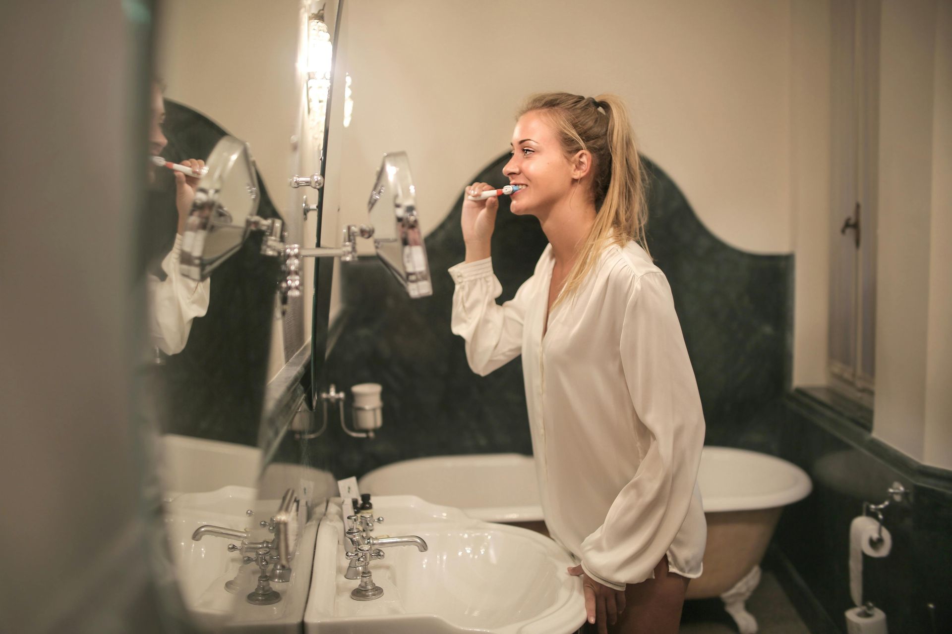 A woman is brushing her teeth in front of a mirror in a bathroom.