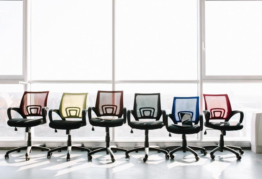 davanti a una finestra sono allineate una fila di sedie da ufficio di diversi colori.