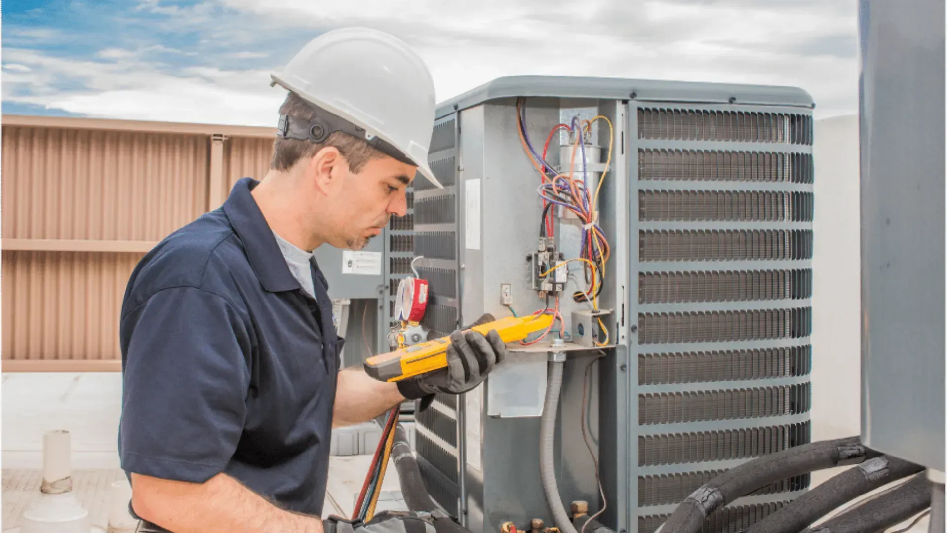 A man wearing a hard hat and gloves is working on an air conditioner.