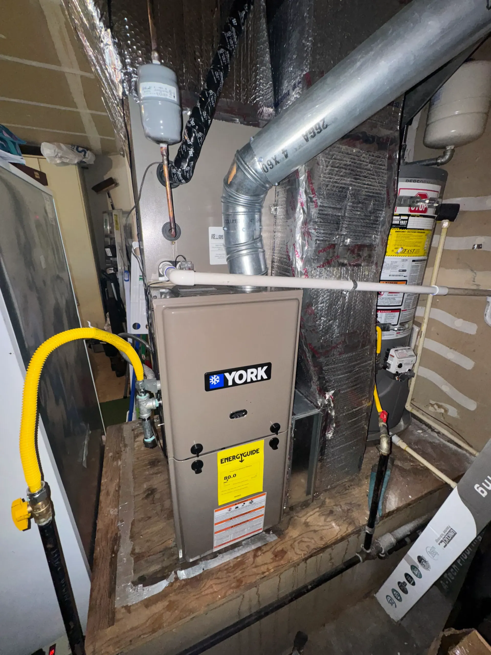 A york air conditioner is sitting in a basement next to a hose.