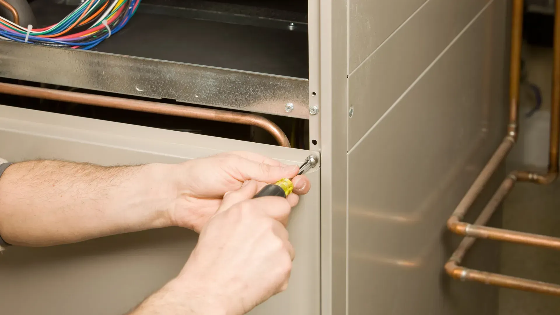A man is working on an air conditioner with a screwdriver.