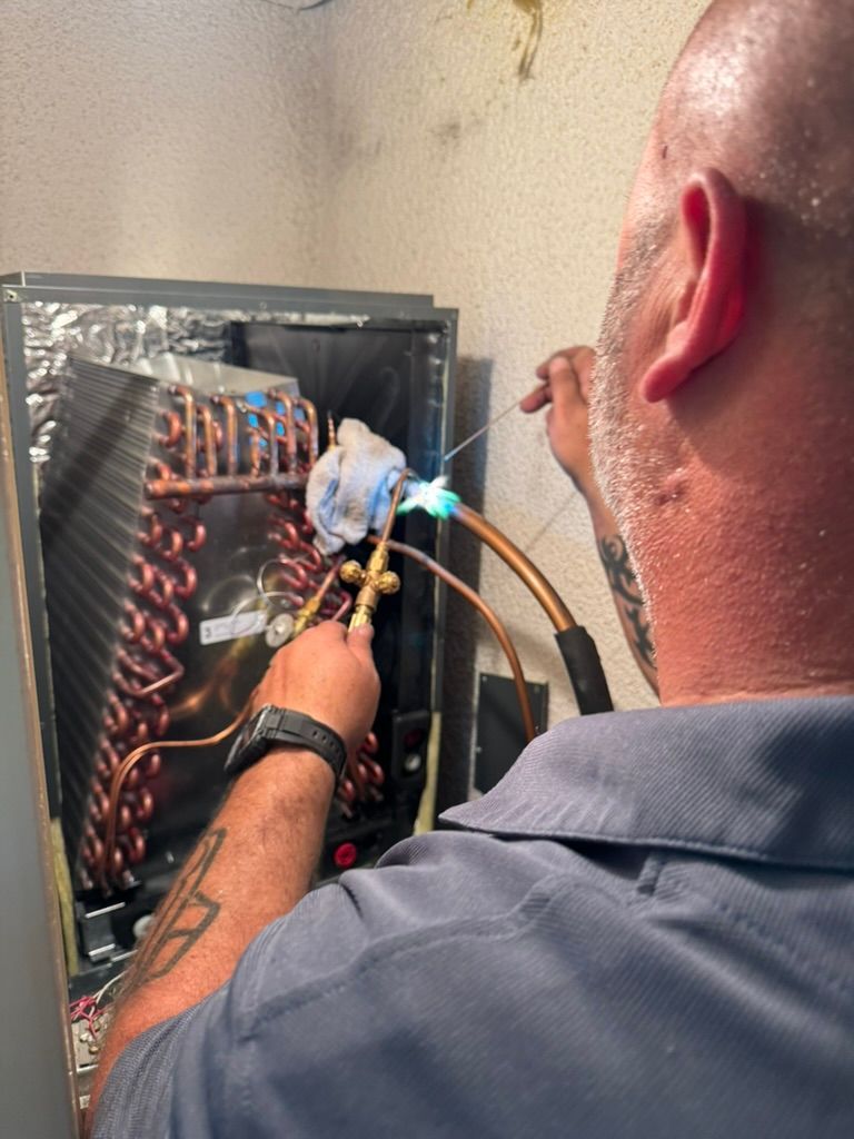 A man wearing a hard hat and gloves is working on an air conditioner.