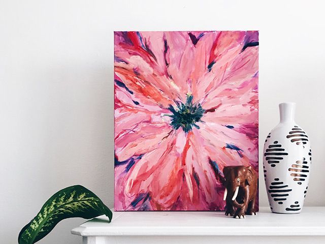 A painting of a pink flower is hanging on a wall next to vases.