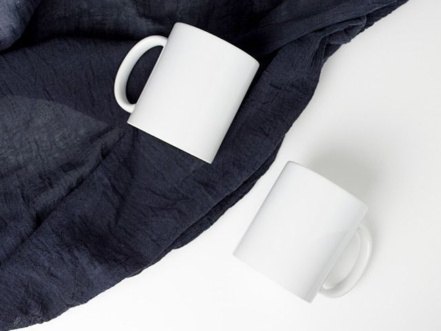 Two white coffee mugs are sitting on a blue cloth