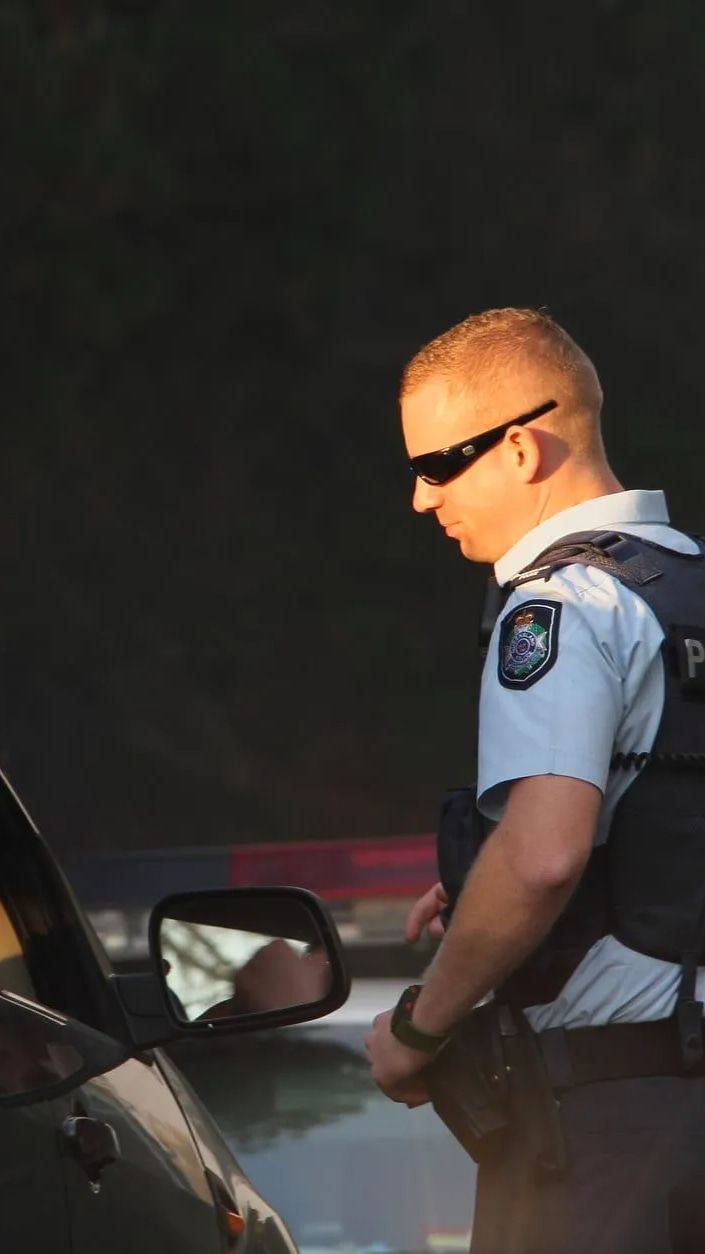 A Man In A Police Uniform Is Standing Next To A Car — Cairns Traffic Lawyers In Cairns City, QLD