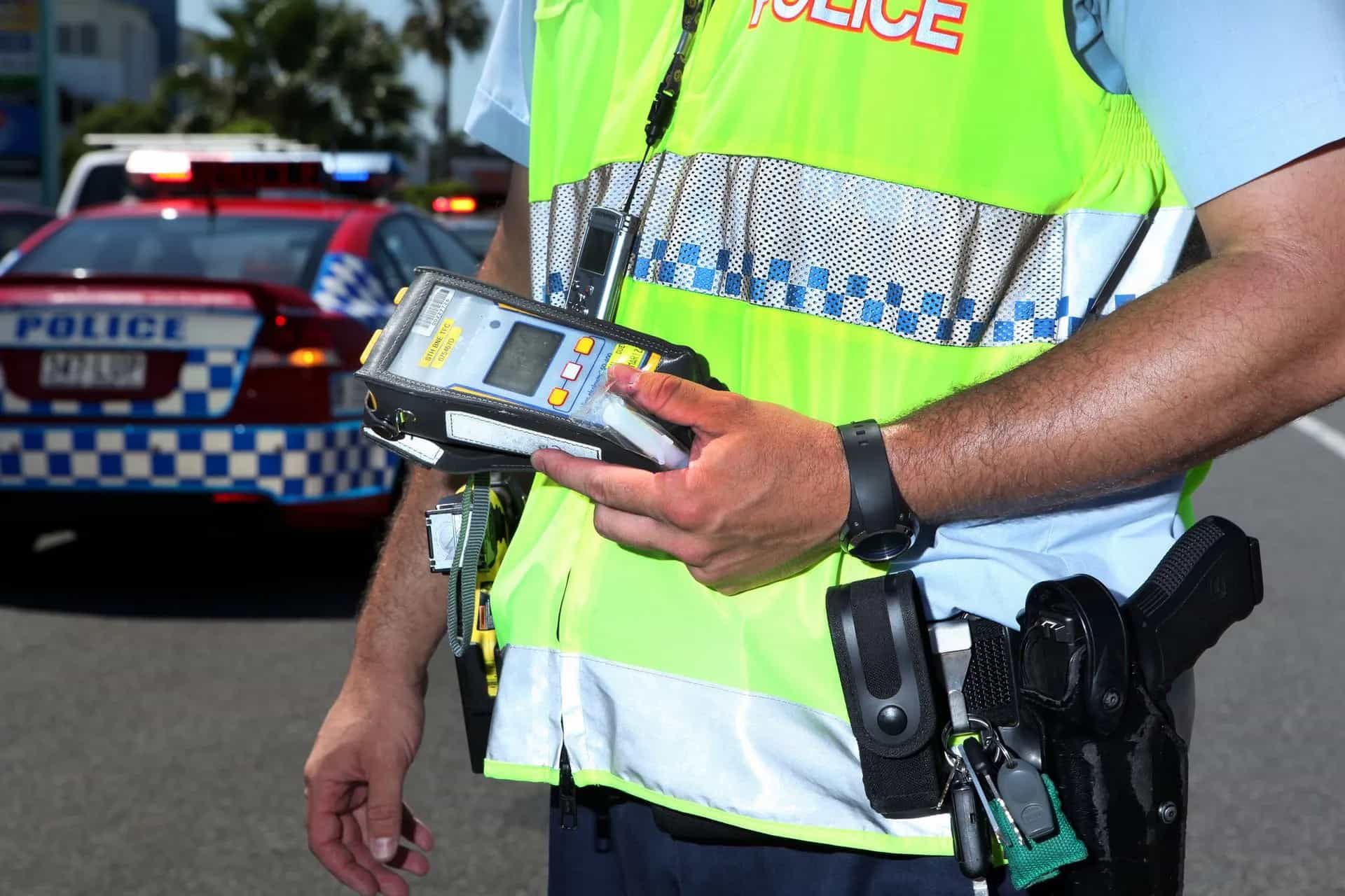 A Police Officer Holding A Breathalyzer — Cairns Traffic Lawyers In Palm Cove, QLD