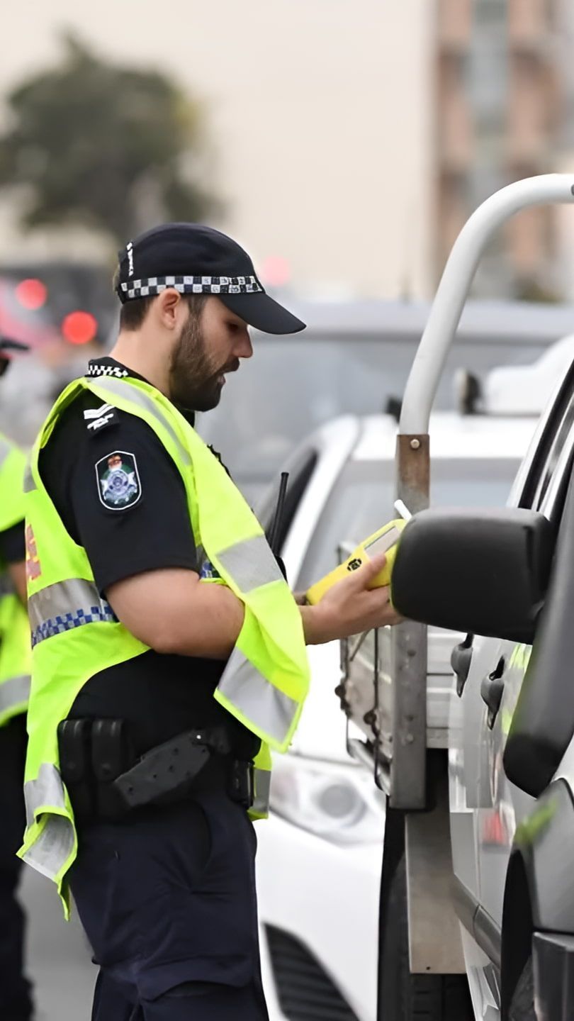 A Police Officer Is Checking The License Plate Of A Car — Cairns Traffic Lawyers In Cairns City, QLD