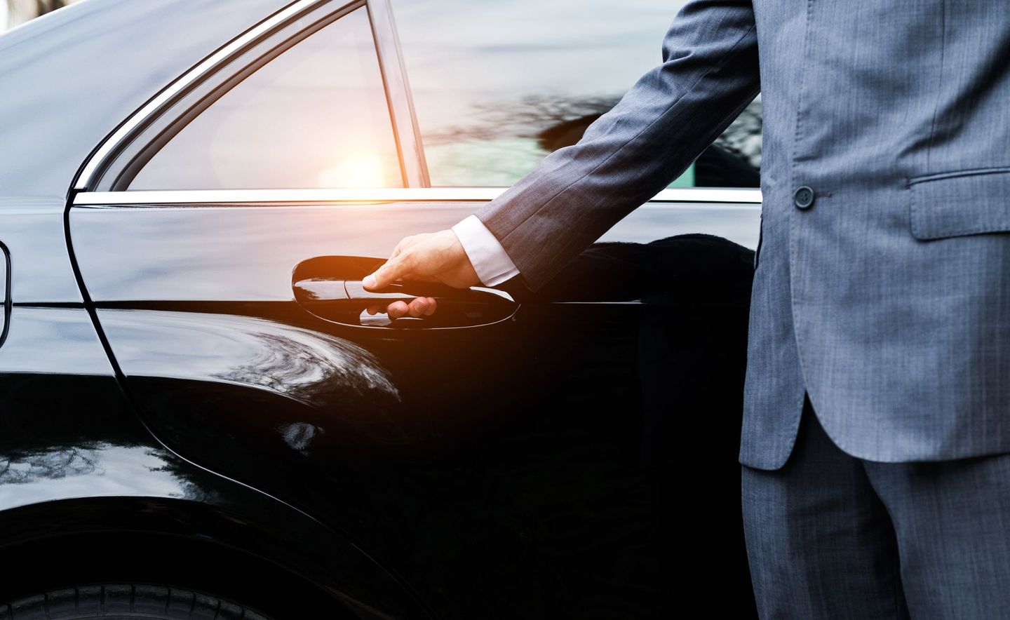 A man in a suit is opening the door of a black car.