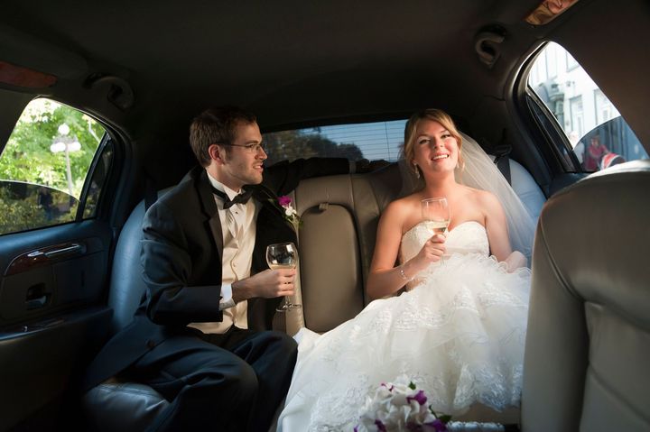 A bride and groom are sitting in the back seat of a limousine.