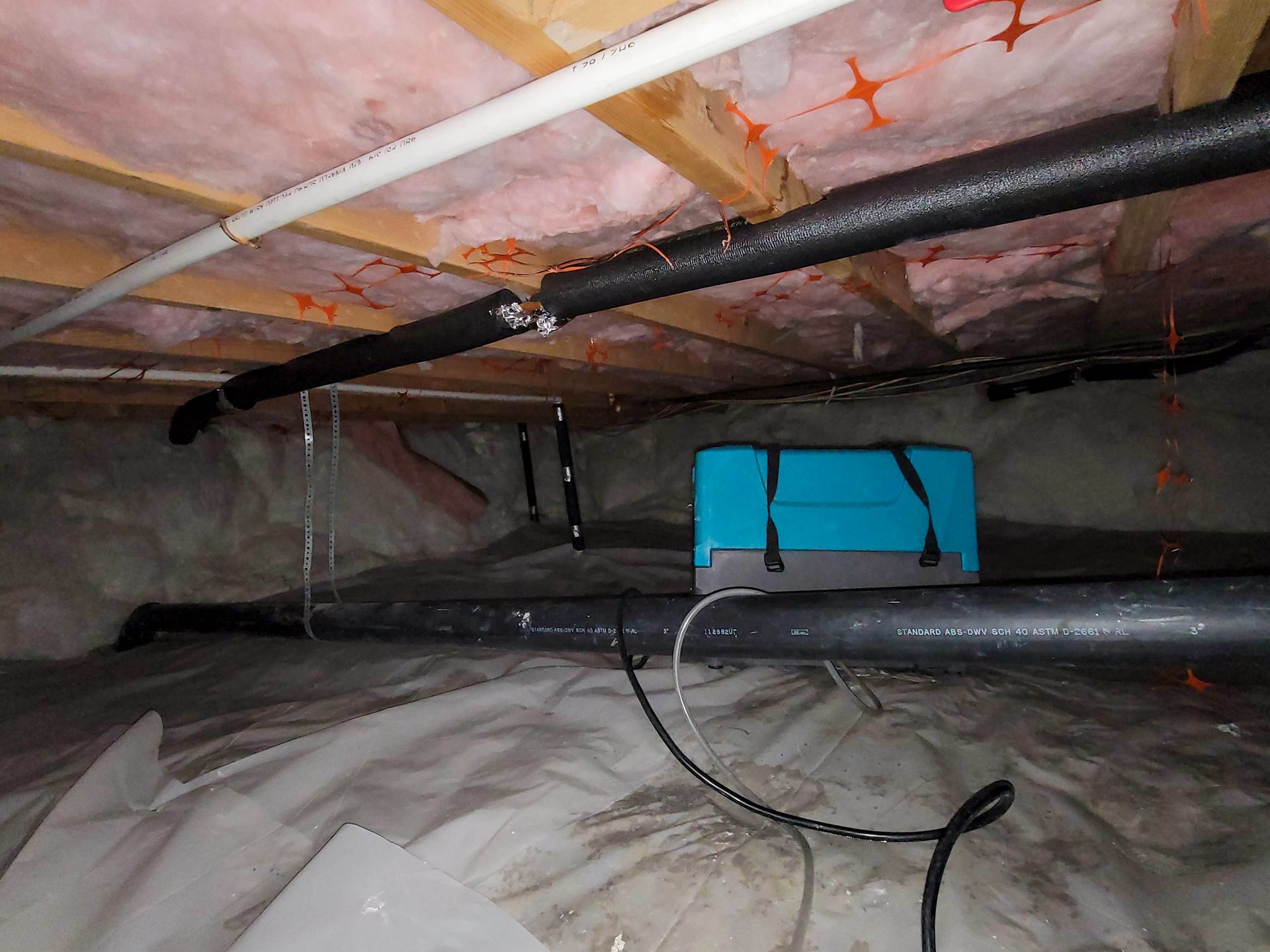 A blue box is sitting under a ceiling in a basement.