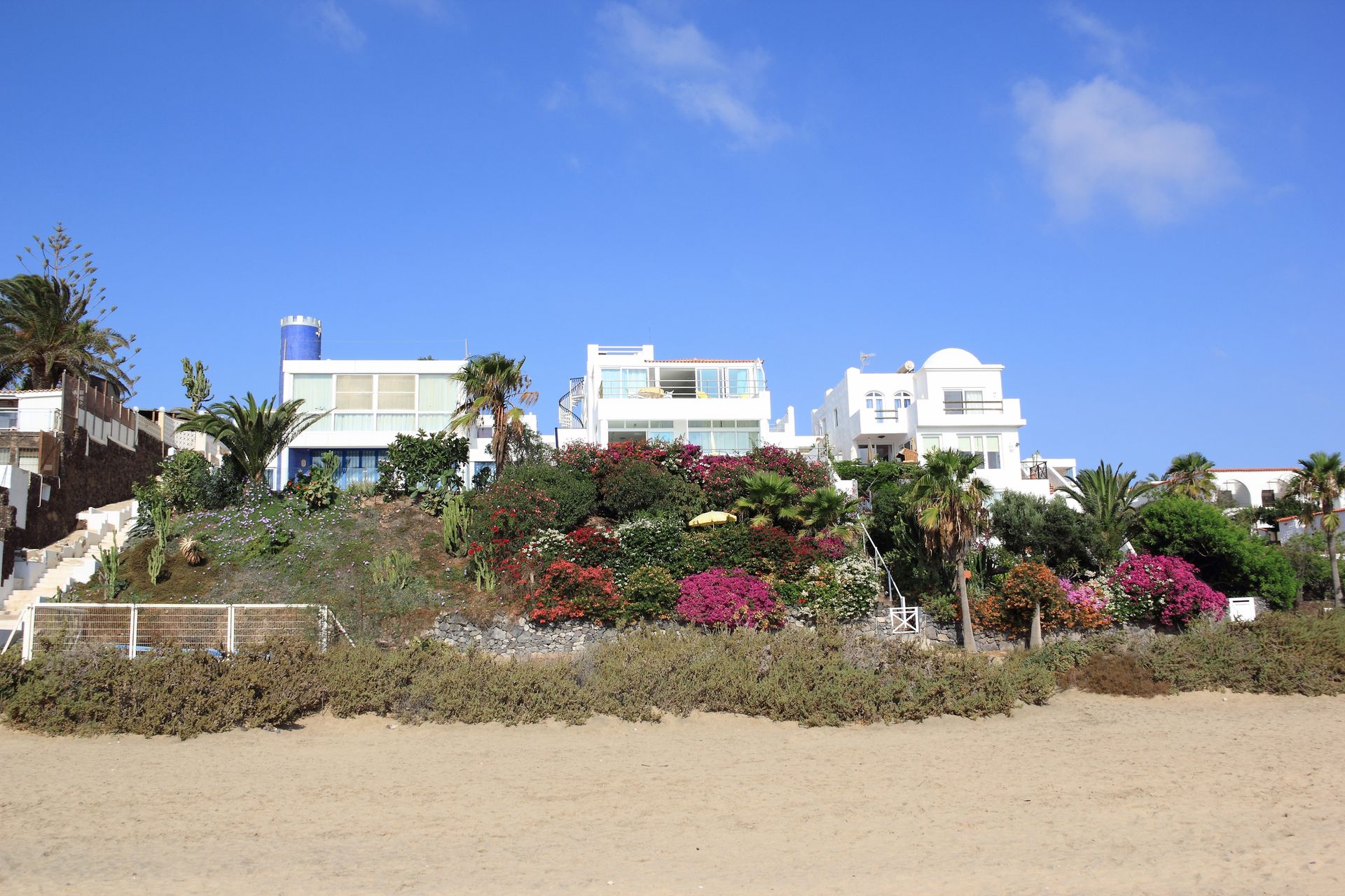 A large white house sits on top of a hill next to a beach