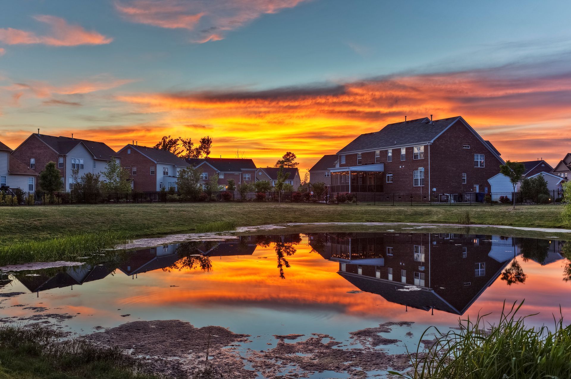 A sunset over a residential area with a pond in the foreground.
