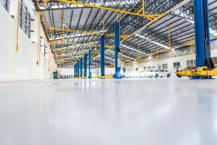 Bright, spacious auto repair shop with blue lifts, white cars, and glossy white floors.