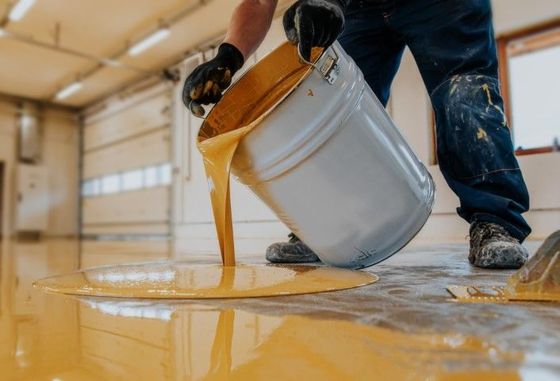 Person pouring yellow epoxy from a bucket onto a garage floor.