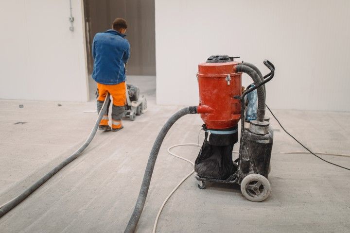 Man using floor grinder, connected to a dust collection system, in a construction area.